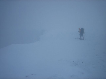 De langgerekte top grenst aan een steile klif, die af en toe door de sneeuwstorm heen zichtbaar is. Deze West Gully gaat 300 meter verticaal omlaag.
